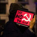 Person holding a protest sign that reads Say NO to CCP with a communist symbol