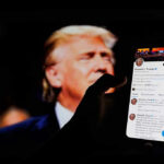 Hand holding smartphone displaying Twitter profile.