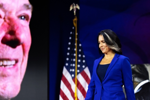 A woman in a blue suit standing on stage with an American flag in the background