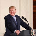 Person speaking at podium, presidential seal on front.