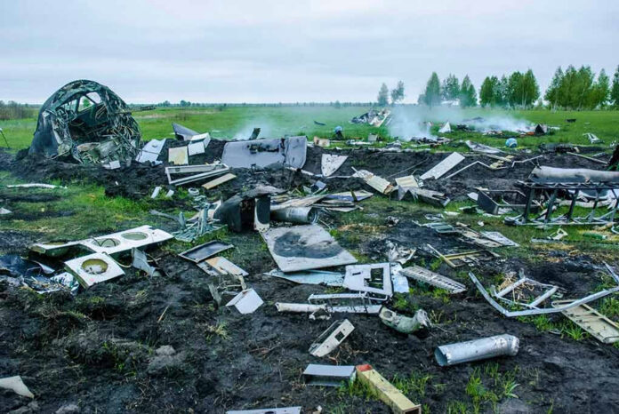 Wreckage of crashed plane scattered across field, smoke rising.