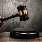 Hand holding judges gavel over sounding block.