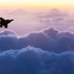 Silhouettes of three fighter jets flying above clouds at sunrise