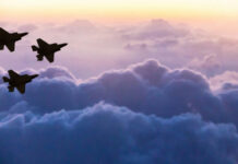 Silhouettes of three fighter jets flying above clouds at sunrise
