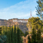 Hollywood Sign on hillside surrounded by trees, clear sky.