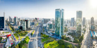 Cityscape with skyscrapers, roads, and green spaces, sunny sky.