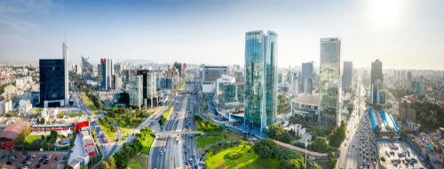 Cityscape with skyscrapers, roads, and green spaces, sunny sky.