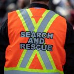 Search and rescue worker in an orange reflective vest seen from behind
