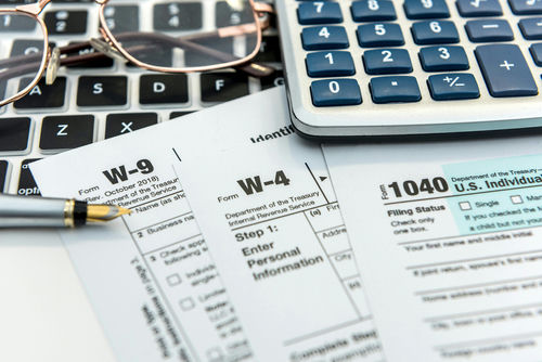 Tax forms with calculator, pen, and glasses on a keyboard