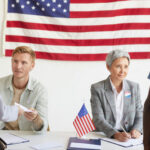Election workers assist voters at a registration table with a U.S. flag behind them