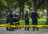 Police officers behind yellow crime scene tape in park.