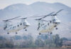 Two military helicopters flying near mountains.