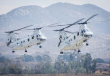 Two military helicopters flying near mountains.