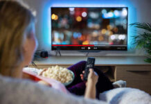 Trump Broadcast Blackout, Licenses Threatened Person watching TV with remote, holding popcorn.