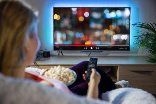 shutterstock1966720738-1jpg Person watching TV with remote, holding popcorn.