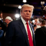 Backroom Deal? Trump Dials Putin, Zelenskyy A serious-looking man in a suit with a red tie surrounded by a crowd and cameras