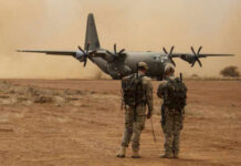 Iran Boasts Strike—Jordan Calls Bluff Two soldiers watch a military transport plane on a dusty airstrip