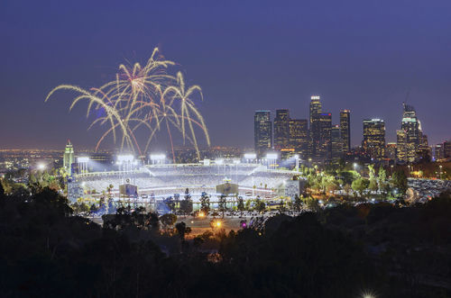 Fireworks above a brightly lit stadium at night with city skyline