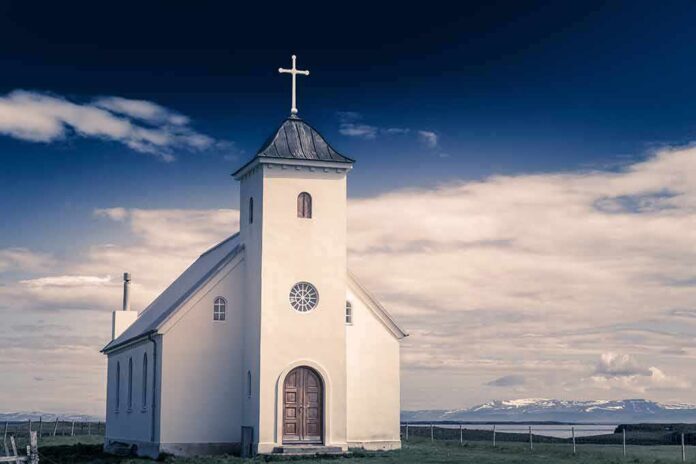 White countryside church with steeple and cross under a dramatic sky