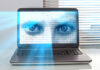 A laptop screen displaying a pair of blue eyes overlaid with binary code