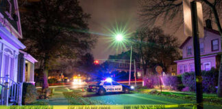 Police car with flashing lights at a crime scene surrounded by caution tape