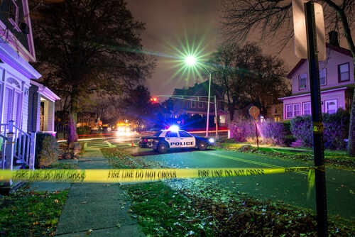 Crime,Scene,With,Tape,And,Police,Car Police car with flashing lights at a crime scene surrounded by caution tape
