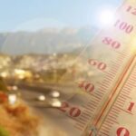 Close-up of a thermometer in hot sun over a blurred road and mountains