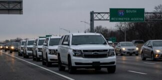A convoy of white SUVs on a highway with a restricted access sign