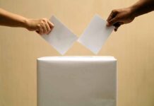 Two hands placing ballots into a voting box.