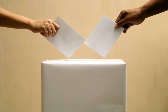 Two hands placing ballots into a voting box.