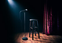 Empty stage with microphone and stool under spotlight.