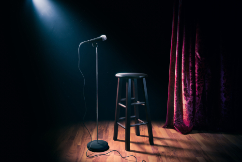 Empty stage with microphone and stool under spotlight.