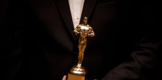 Person holding an Oscar statuette in formal attire.