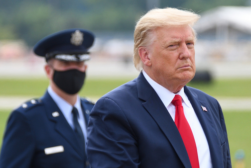 Donald Trump in suit with military personnel behind him.