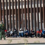 Border patrol agent with group of seated immigrants.