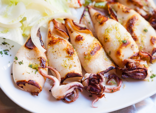 Grilled squid garnished with herbs and served with onions.