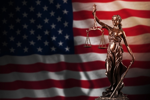 Lady Justice statue with scales, American flag background.