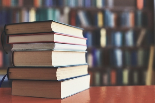 Stack of books on table with blurred bookshelf background.