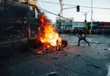 Person near large street fire during protest.