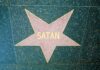 Pink star with Satan on green speckled pavement.